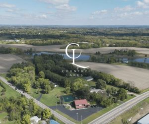 Aerial view of farmland, ponds, and wooded areas with a large white Country Lakes logo centered on the image.